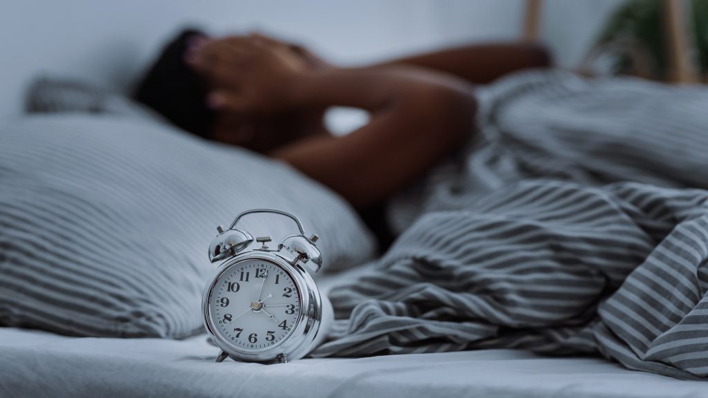 Image of person lying in bed with clock in foreground